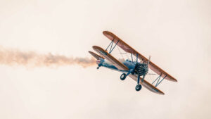 Ein alter Doppeldecker, eine Boeing Stearman Pt-13D, zieht eine Rauchfahne hinter sich. Hier wird ein Luftkampf bei einer Flugshow simuliert.